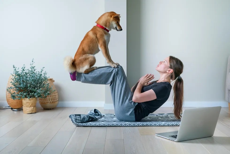 Image of a dog perched on a woman's shins as she does a yoga pose